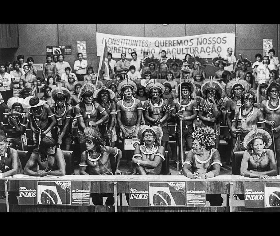 À frente na bancada, da esquerda para a direita: Teseya Panará, Kanhõc Kayapó, Raoni Mētyktire e Tutu Pombo Kayapó, dentre outros, ocupam auditório da liderança do PMDB nas negociações do capítulo dos indígenas na Constituinte, Brasília, 31.05.1988 À frente na bancada, da esquerda para a direita: Teseya Panará, Kanhõc Kayapó, Raoni Mētyktire e Tutu Pombo Kayapó, dentre outros, ocupam auditório da liderança do PMDB nas negociações do capítulo dos indígenas na Constituinte, Brasília, 31.05.1988
